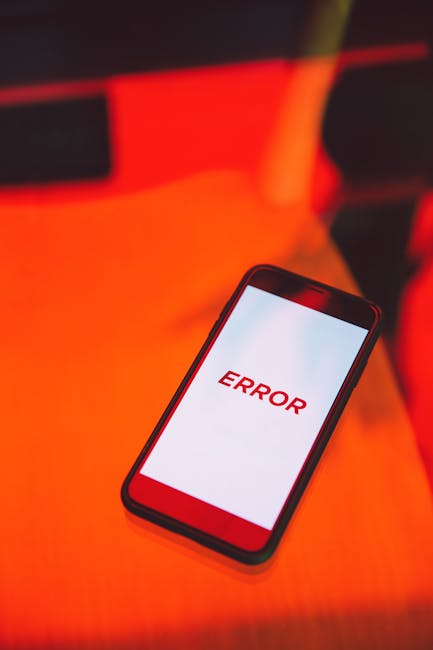 A close-up image of a smartphone lying flat on a surface, displaying a prominent red error message on the screen. The surrounding area is illuminated with a red and orange glow, suggesting low ambient