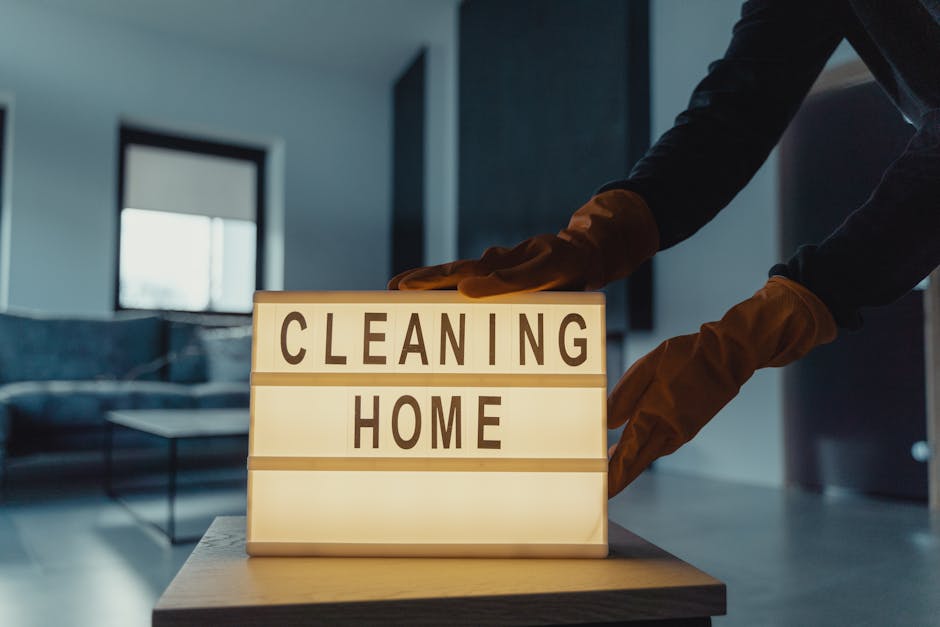 A professional cleaner from Hammersmith Carpet Cleaners, dressed in black and white uniform with gloves, is carefully folding and arranging white towels on a dark-colored table in a well-lit, elegant 