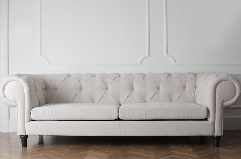 Close-up of a person vacuuming a decorative yellow and white patterned cushion on a dark fabric sofa, focusing on surface cleaning and upholstery maintenance in a residential living room, with soft li